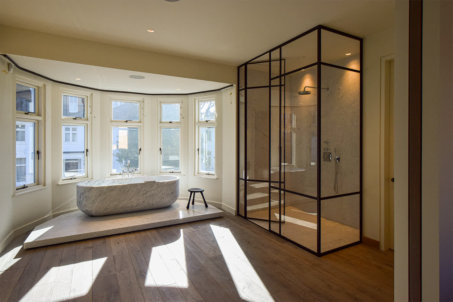 bespoke full-height glass shower enclosure with bronze frame next to a freestanding stone bathtub in a luxury bathroom