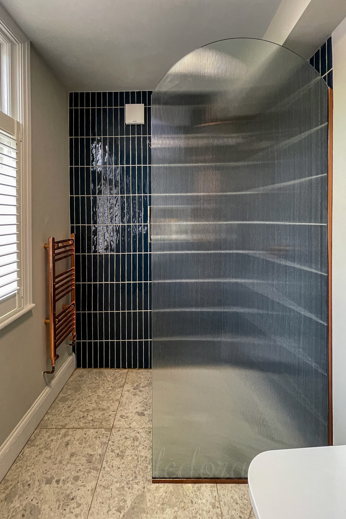 Arched glass shower screen with fluted privacy glass and curved frameless top in a London bathroom