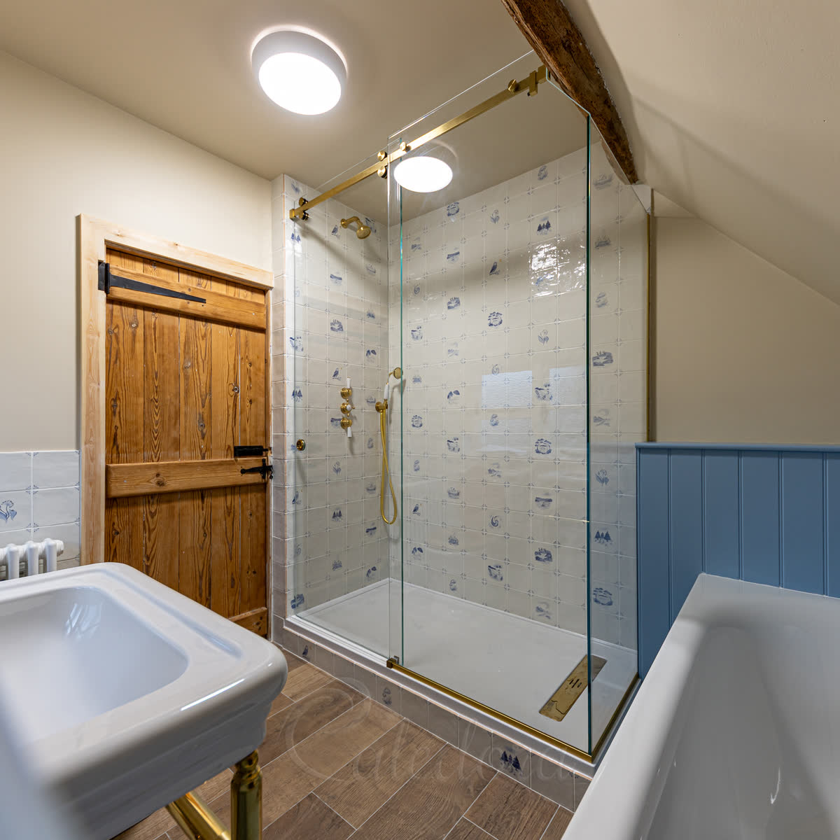 Sliding glass shower enclosure with brushed brass track, glass shaped to sloped loft ceiling and joist notch — fitted workshop precision