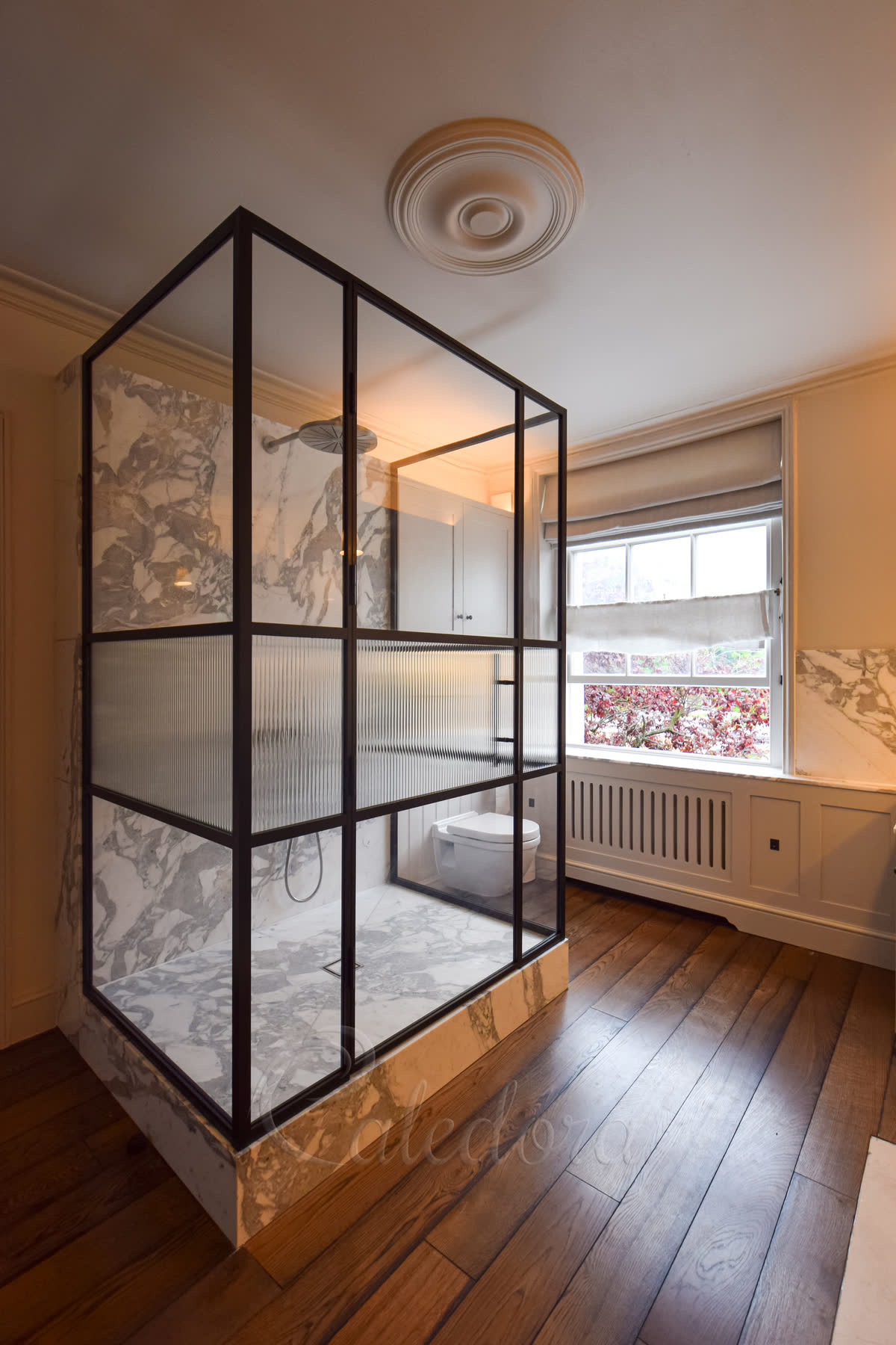 Luxury three-sided shower enclosure with black grid frame and fluted glass panels in marble bathroom